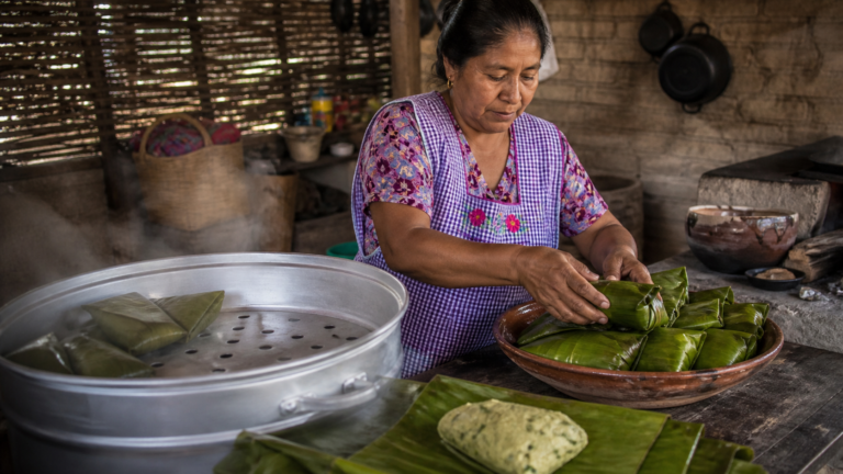 Cocinera tradicional acomoda tamales de chipilín envueltos en hojas dentro de una vaporera.